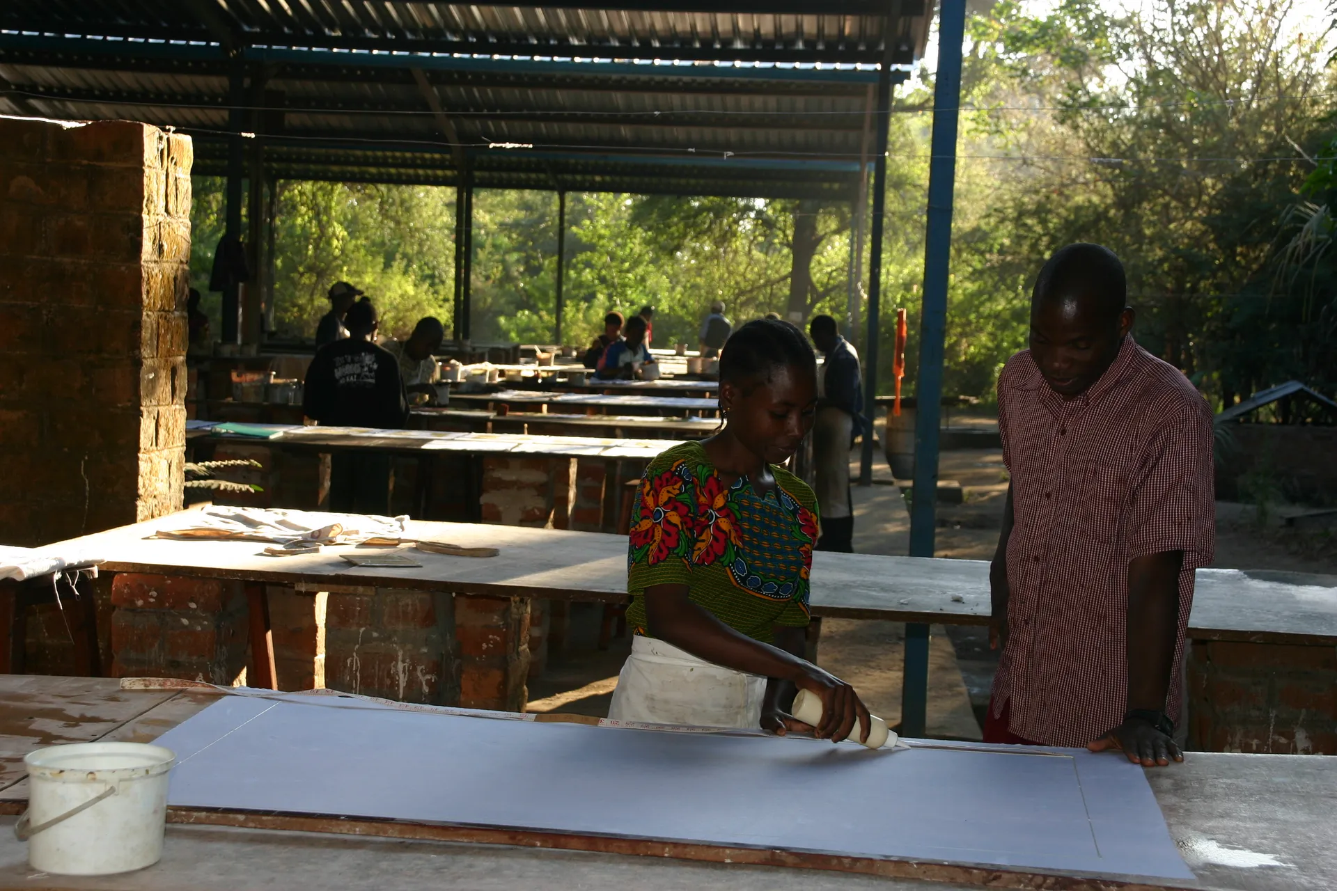 In de open hal tekenen arbeiders bij <i>Tribal Textiles</i> de patronen op het katoenen doek [Mfuwe]