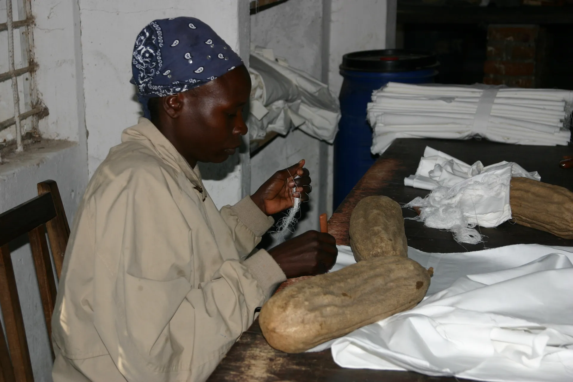 De vruchten van de <i>saucage tree</i> houden de lap tegen terwijl de vrouw rafelrandjes maakt [<i>Tribal Textiles</i>, Mfuwe]