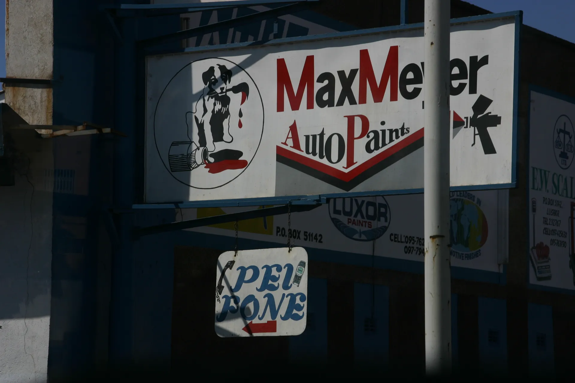 Reclame langs de weg, let bij de telefoonreclame op de schrijfwijze van <i>Pay Phone</i> [Lusaka]