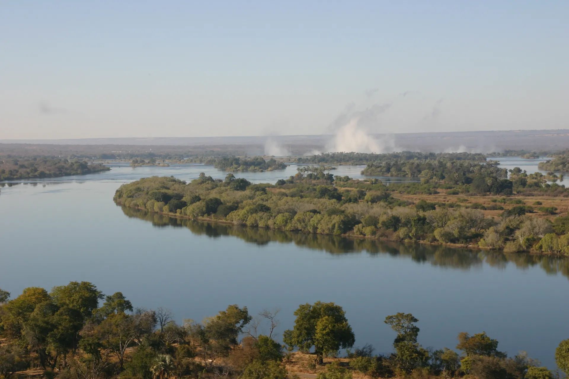 Boven het kalme water van de Zambezi is in de verte <i>de rook die dondert</i> zichtbaar [Victoria watervallen]