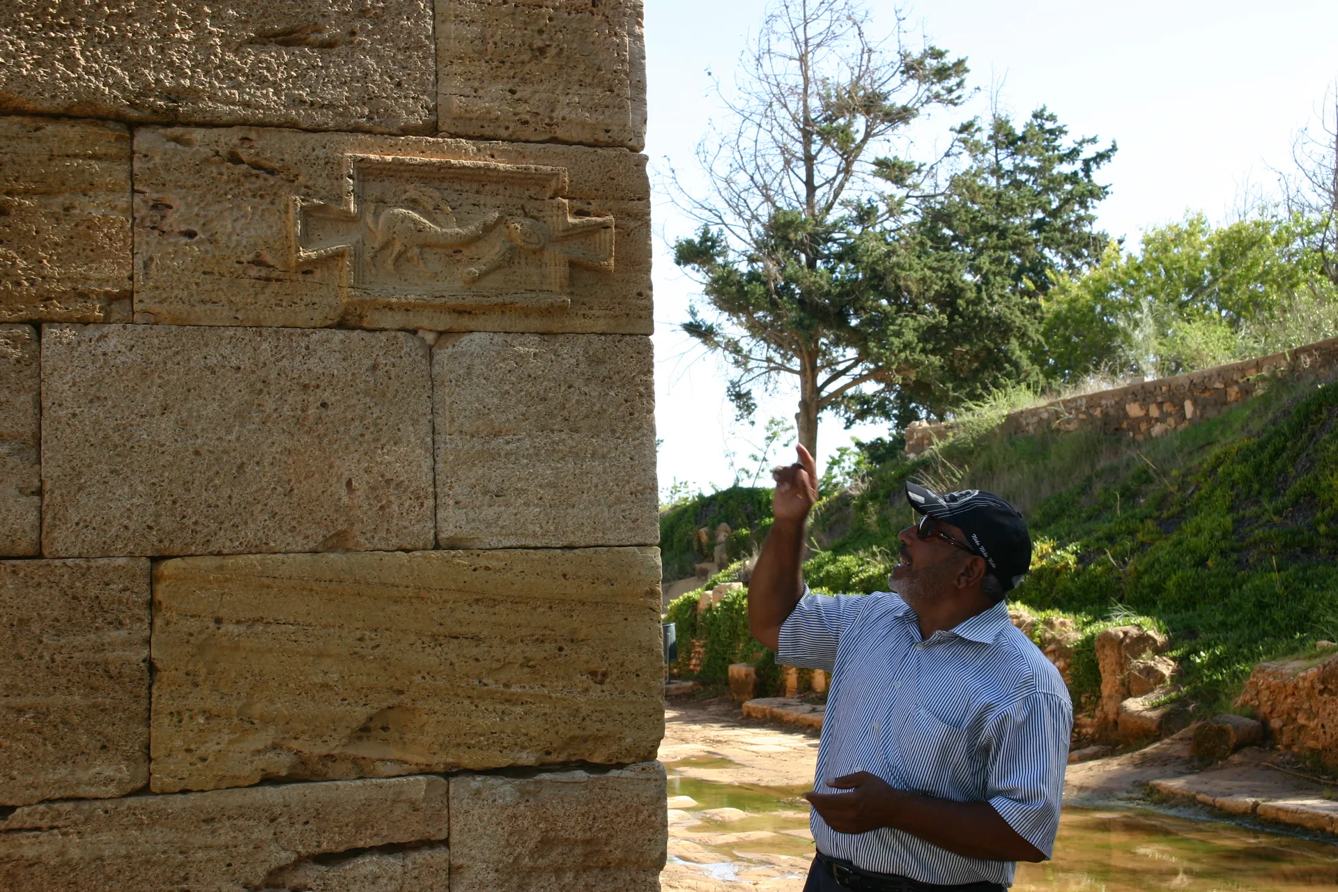 Onze gids Abdullah geeft uitleg over de <i>tabula ansata</i> met kwaadafwerende tekens [Leptis Magna]