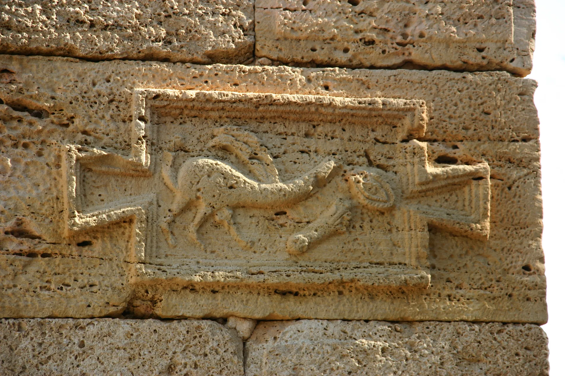 Op de straathoek hangt een <i>tabula ansata</i> met kwaadafwerende tekens, waaronder een fallus [Leptis Magna]