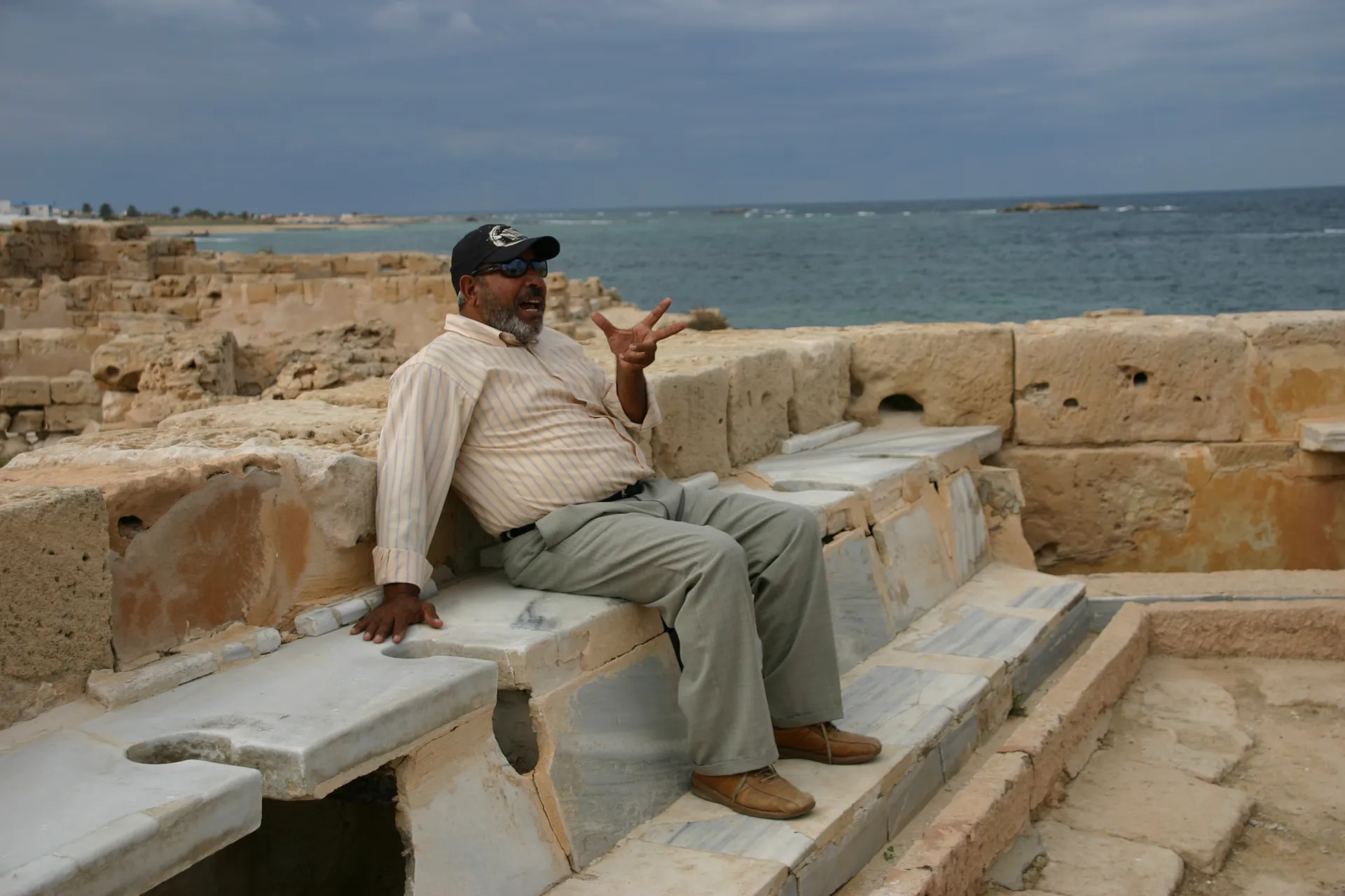 Gezeten op een Romeins toilet geeft onze gids Abdullah uitleg [Sabratha]